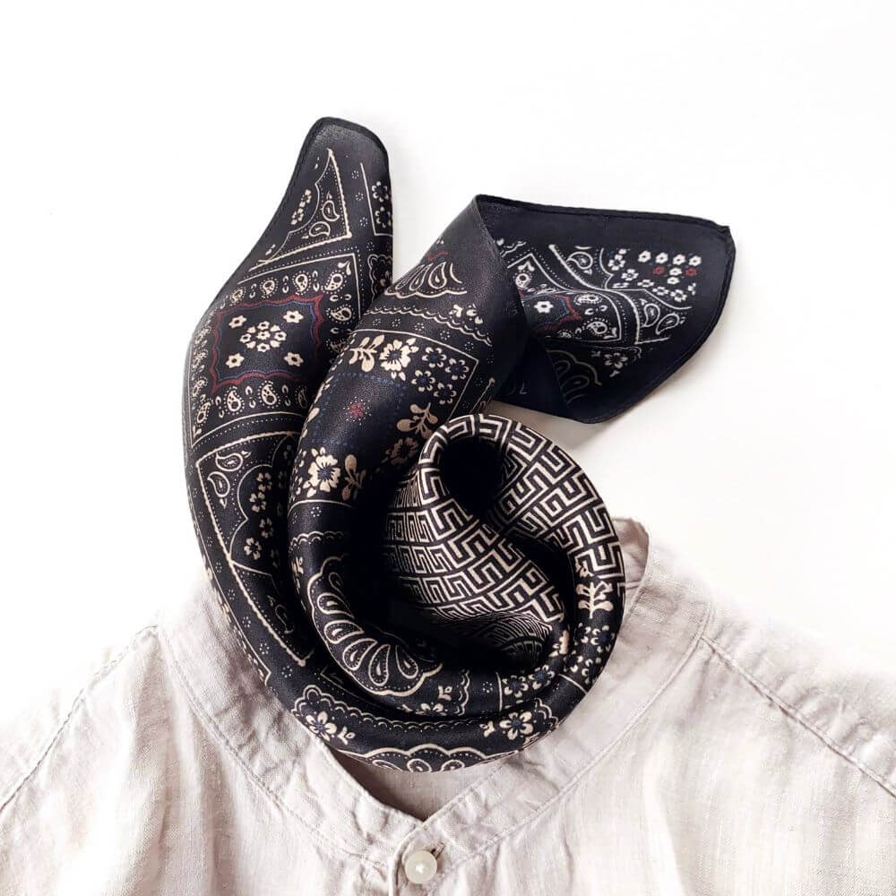 Black geometric floral silk square scarf folded and placed on linen top