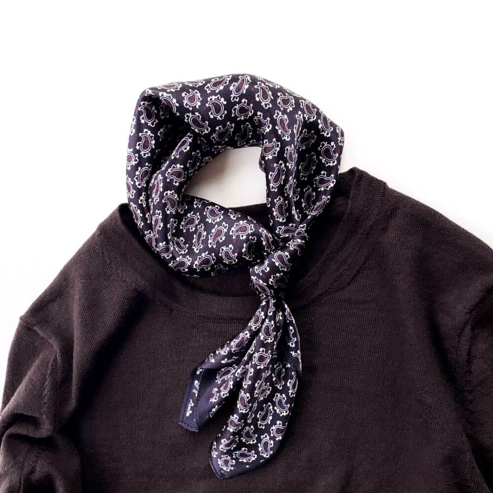 Dark purple paisley silk square scarf tied in a simple knot on a sweater