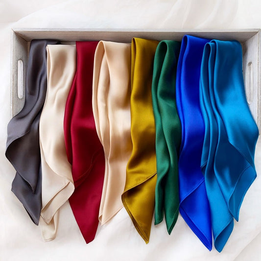 multi colours mulberry silk square scarves arranged side-by-side inside a grey wooden tray. The colours are dark grey, ivory cream, berry red, champagne beige, gold olive, emerald green, royal blue and kingfisher blue.