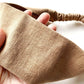 Close-up of a hand holding a taupe brown linen headband on a white background