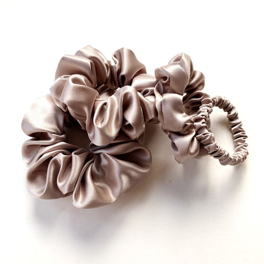 Four taupe mulberry silk satin scrunchies and hair ties on a white background
