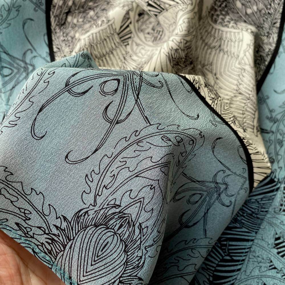 Close-up of teal, black and ivory illustrated mulberry silk crepe de chine scarf showing detailed line-art patterns.