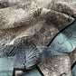 Close-up of teal, black and ivory illustrated mulberry silk crepe de chine scarf showing detailed line-art patterns.