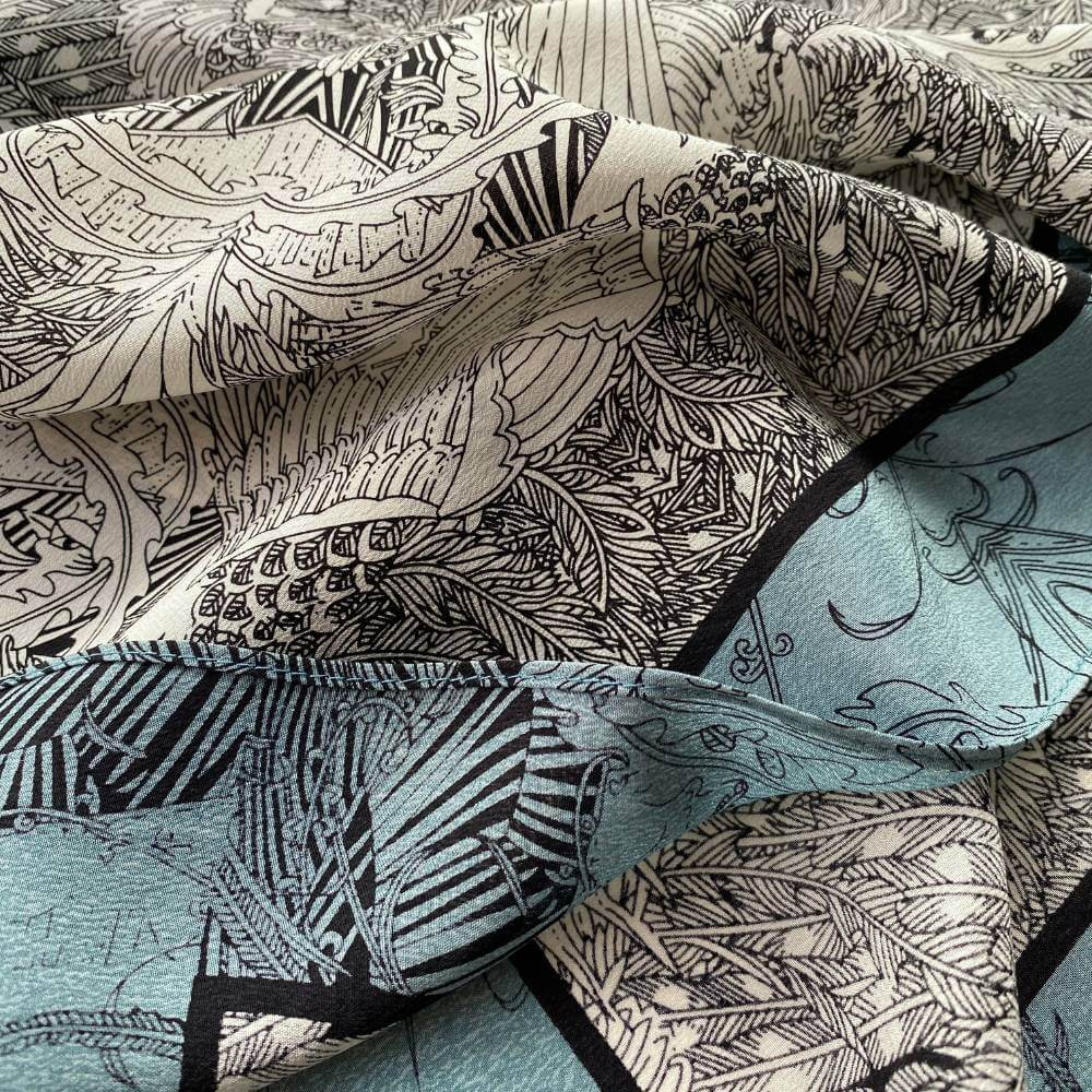 Close-up of teal, black and ivory illustrated mulberry silk crepe de chine scarf showing detailed line-art patterns.