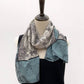 Teal, black and ivory illustrated long silk scarf styled on a mannequin over a black top.