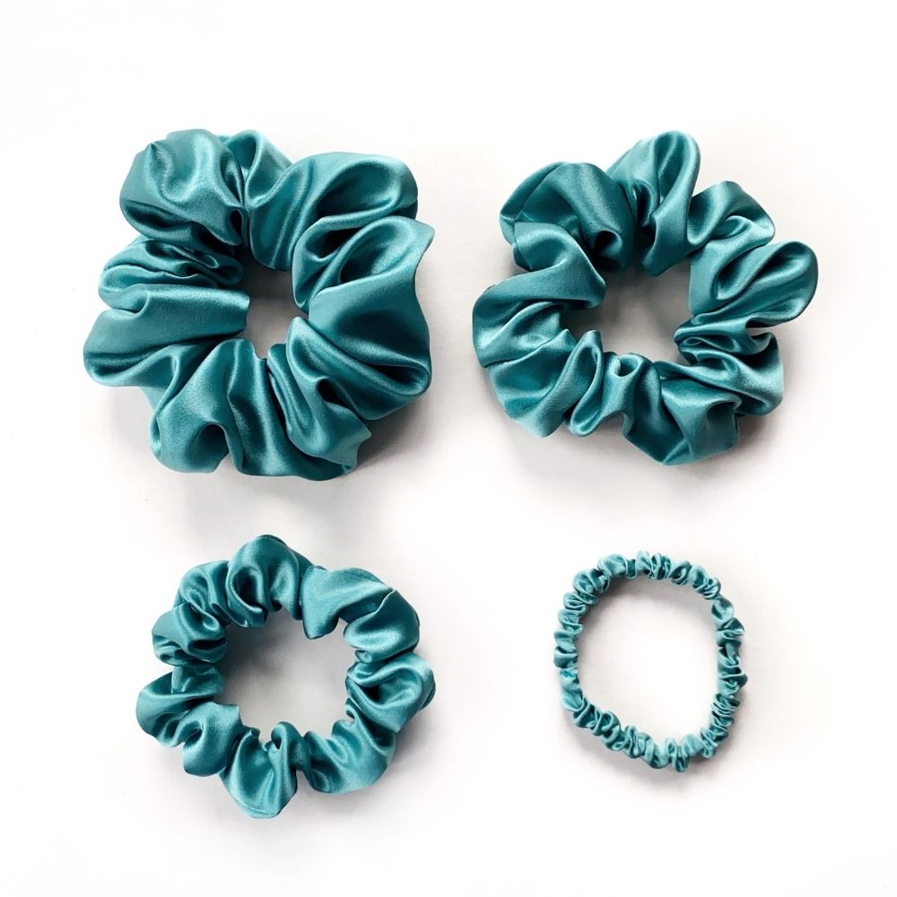Set of teal blue pure mulberry silk satin scrunchies and hair ties on a white background