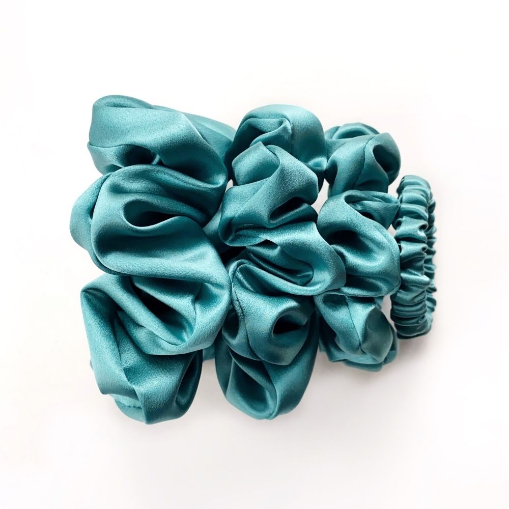 Set of teal blue pure mulberry silk satin scrunchies and hair ties on a white background