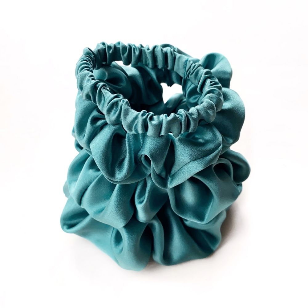 Set of teal blue pure mulberry silk satin scrunchies and hair ties on a white background
