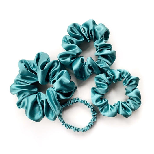 Set of teal blue pure mulberry silk satin scrunchies and hair ties on a white background