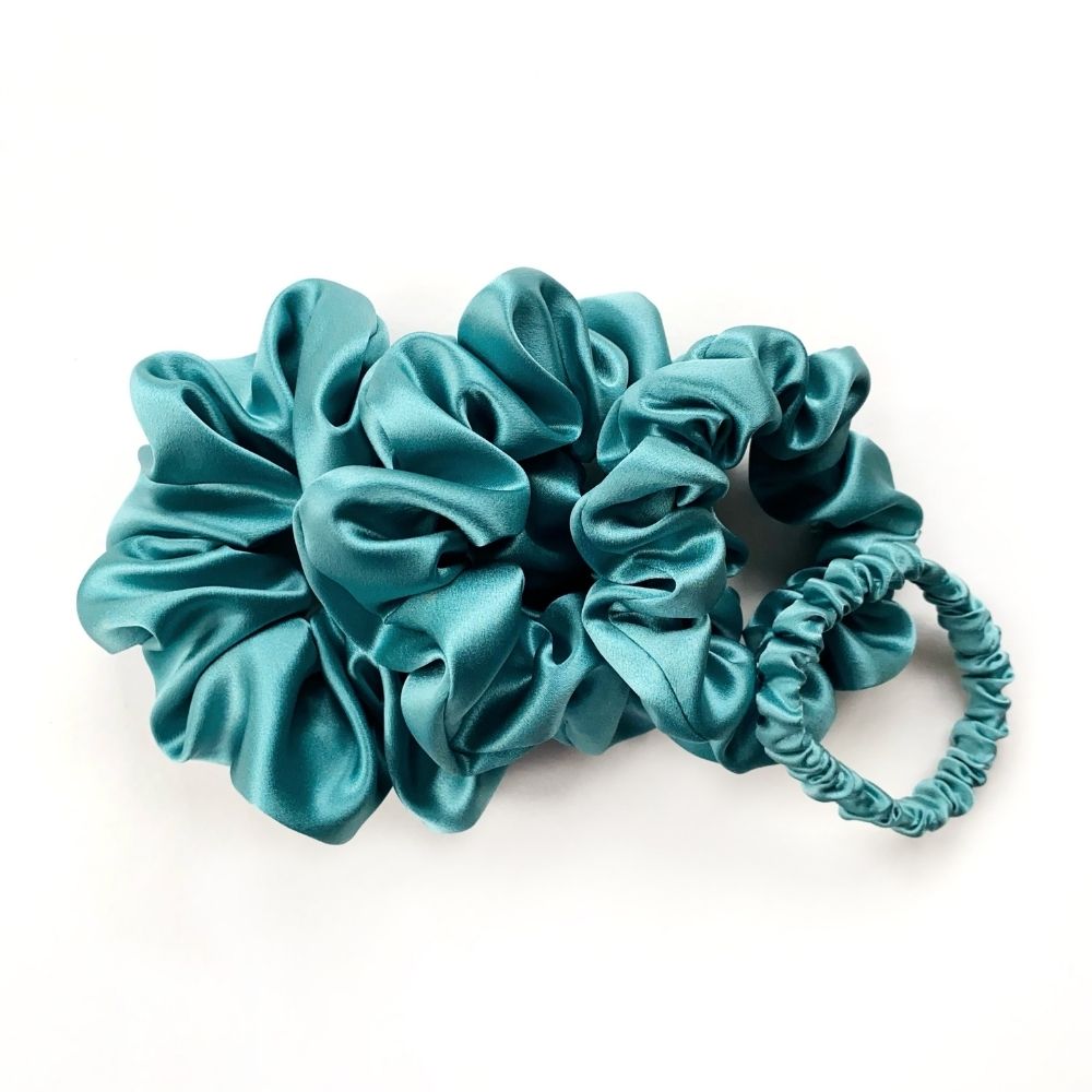 Set of teal blue pure mulberry silk satin scrunchies and hair ties on a white background