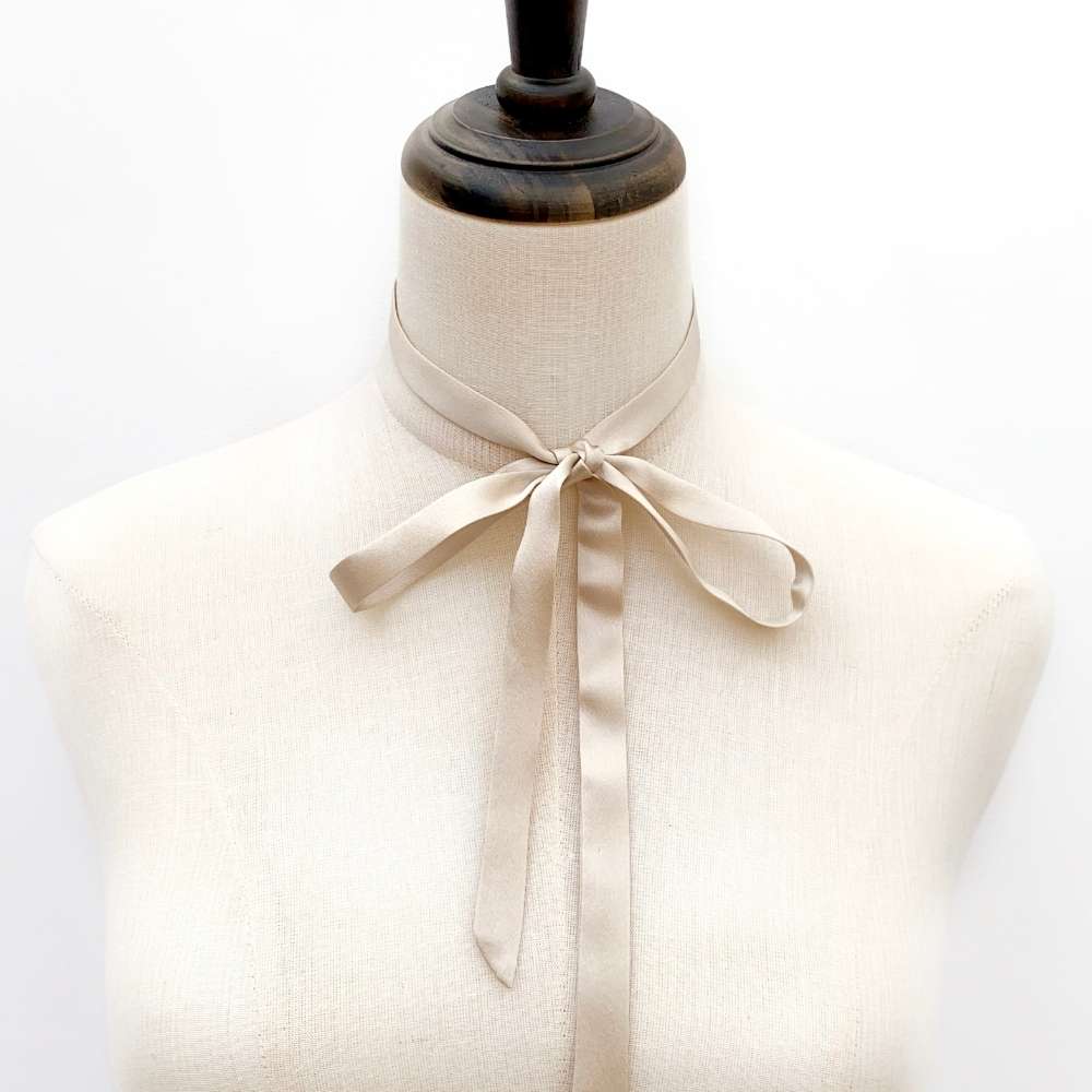 Mannequin wearing a champagne Beige mulberry silk ribbon scarf into a bow tie on a white background