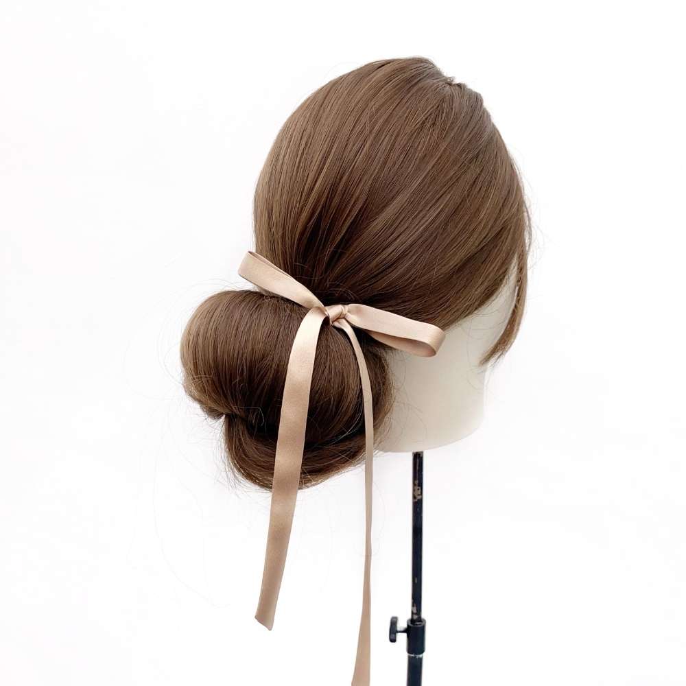 Mannequin head with brown hair styled in a bun with a khaki silk ribbon hair tie on a white background