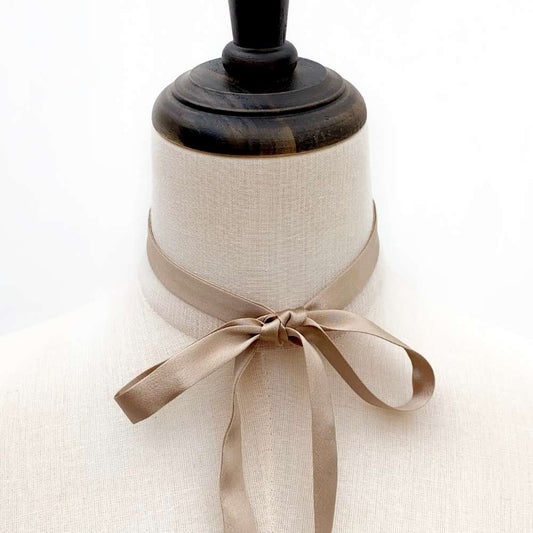 Mannequin bust with a Khaki mulberry silk ribbon tied around its neck on a white background