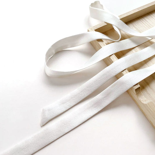 White skinny mulberry silk ribbon on a wooden surface with a white background