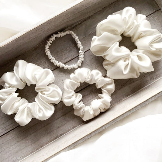 Set of white mulberry silk satin scrunchies and silk hair ties on a wooden surface