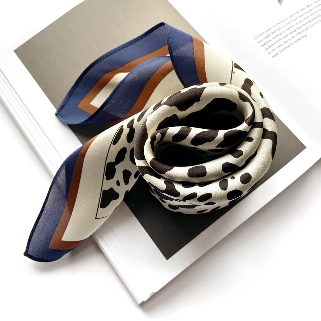 wrapped black leopard print ivory mulberry silk square scarf with blue and brown border on top of a book.