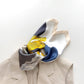 yellow blue and white coloured mulberry silk square neck scarf with abstract patterns draped over a beige garment on a light background