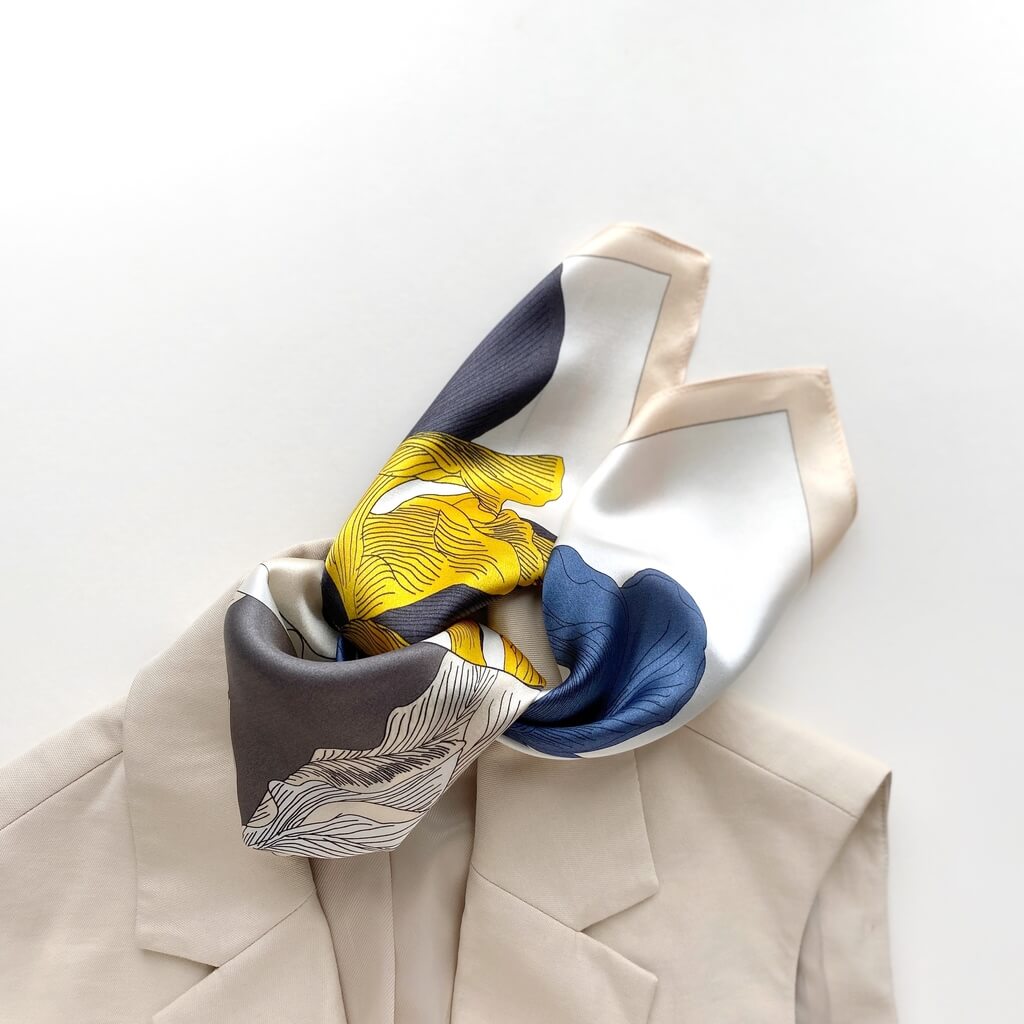 yellow blue and white coloured mulberry silk square neck scarf with abstract patterns draped over a beige garment on a light background